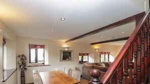 A dining area with a wooden table and chairs, a staircase with wooden balusters, and a mirror on the wall. - Woodside Barn (Ulverston)