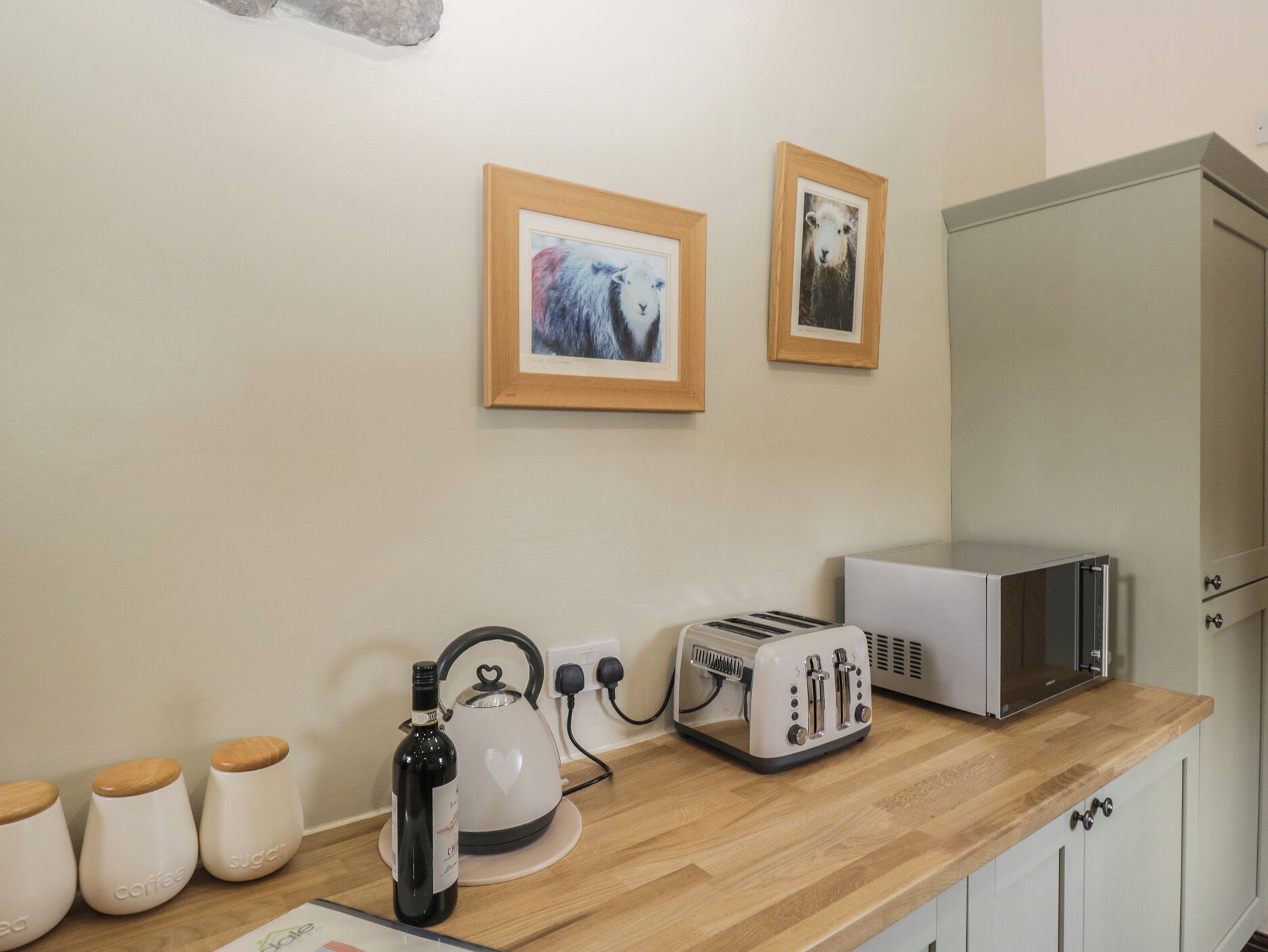 Eine Küche mit Toaster, Wasserkocher und Kaffeebehältern. An der Wand hängen zwei gerahmte Bilder.