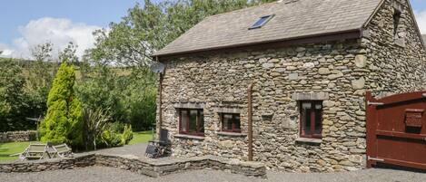A stone building with a sloped roof, two windows with red frames, a satellite dish, and a gravel driveway.