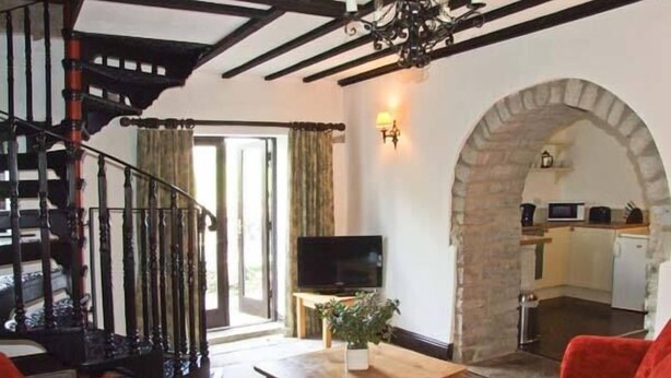 A living room with a red sofa, a wooden coffee table with a plant, a TV, and a staircase with a black railing. - The Cottage (Buxton)