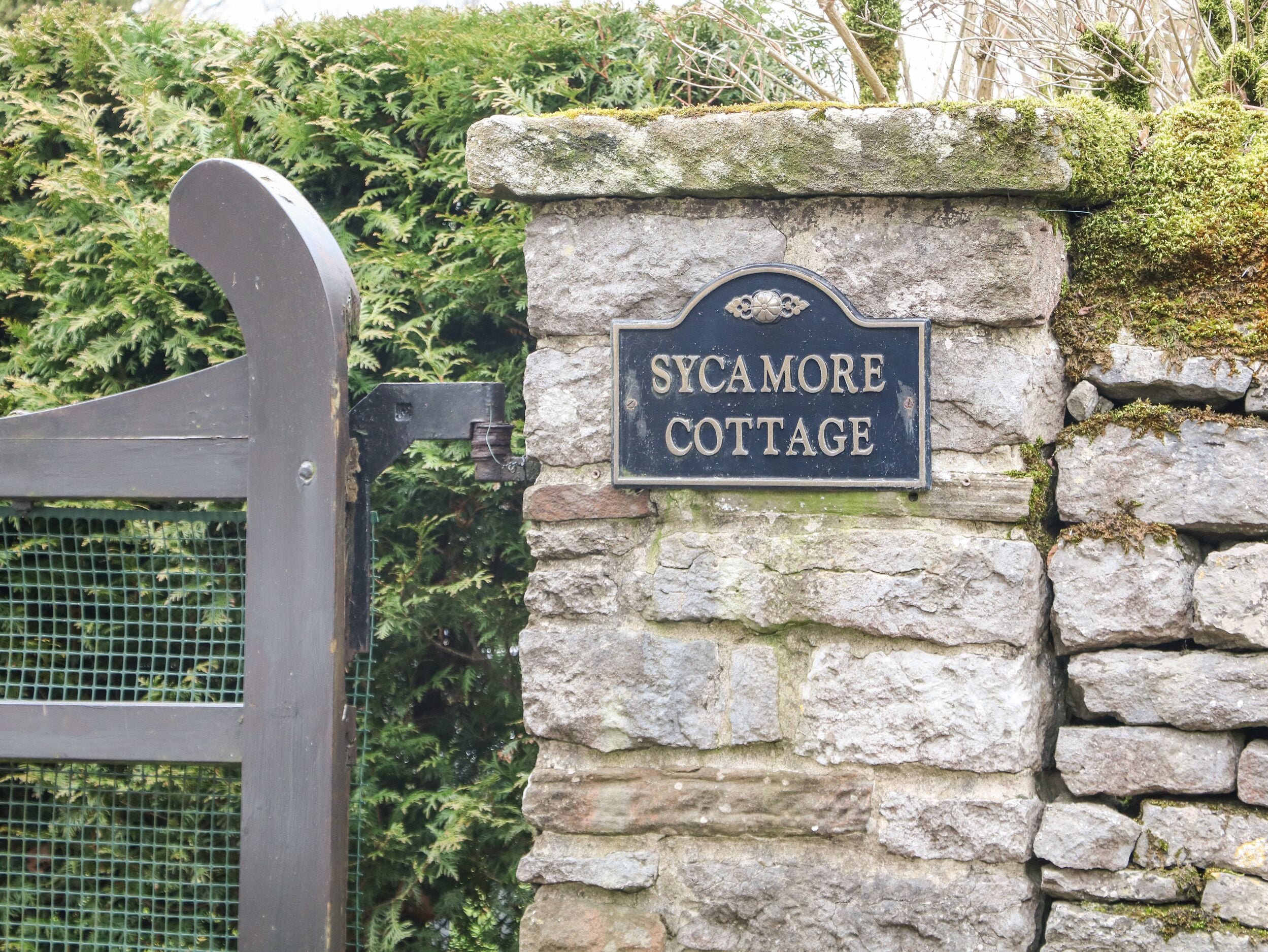 En stenmur med en skylt som visar texten ”Sycamore Cottage”.