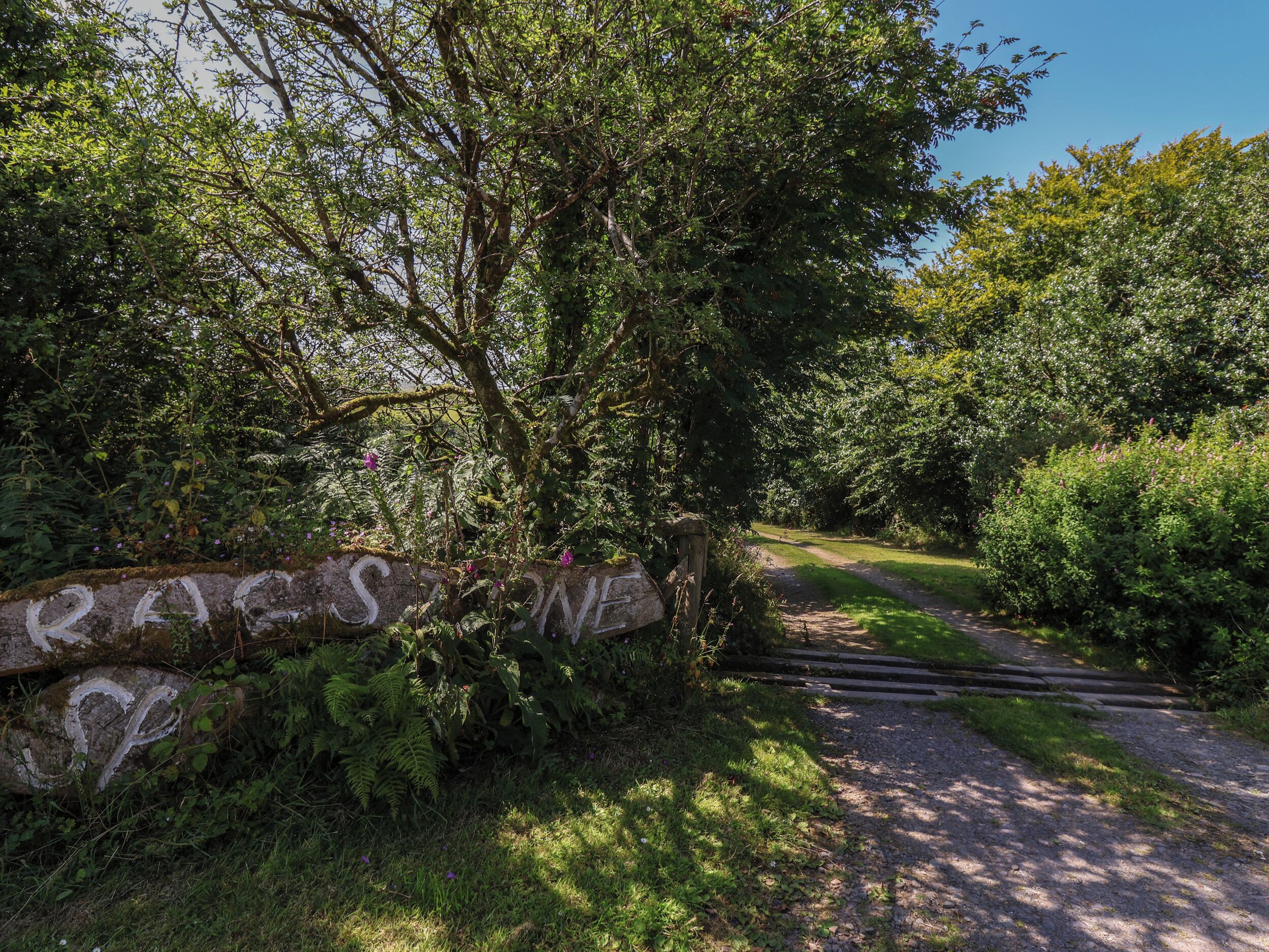 A stone sign with the inscription "RALES SONE" at the entrance of a garden path.