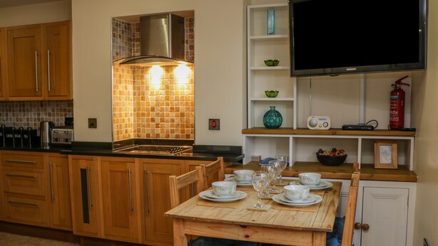 A modern kitchen with wooden cabinets, a tiled backsplash, a built-in stove, and a dining area with a table set for four. - Apartment 6 (Whitby)