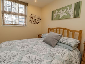 Een slaapkamer met een bed, een raam met zonwering, een kunstwerk aan de muur en een nachtkastje.
