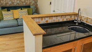 A kitchen with a black countertop, wooden cabinets, and a tiled backsplash. - Apartment 6 (Whitby)