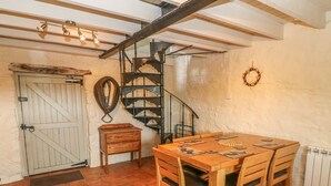 Un comedor rústico con una mesa y sillas de madera, una escalera en espiral y una puerta blanca con picaporte de madera.