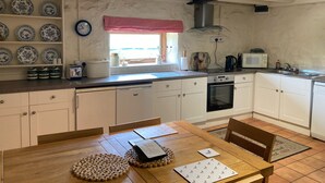Una cocina con armarios blancos, una mesa de comedor de madera y un ventanal con un adorno rojo.