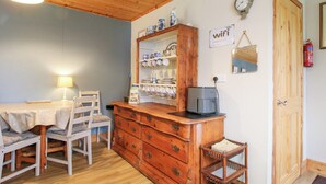 A cozy room with a wooden dresser, a dining table with chairs, a coffee maker, and a clock on the wall. - The Log Cabin (Craven Arms)