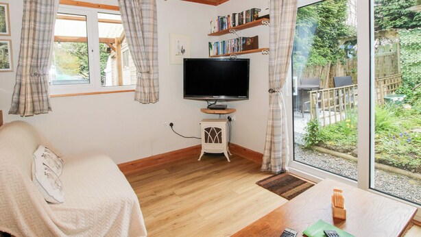 A cozy living room with a television, bookshelves, and a large window with curtains. - The Log Cabin (Craven Arms)