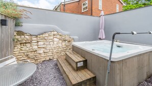 Un jacuzzi con escalones, una mesa y un muro de piedra en un patio trasero.