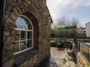 A stone building with a large arched window, outdoor patio with a table and chairs, and a green umbrella. - The Old Mill (Grange-over-Sands)