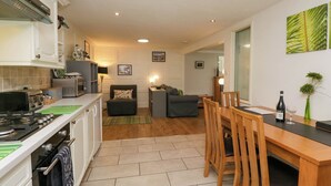 A compact kitchen with a stove, microwave, and cabinets. There is a dining area with a table and chairs, and a living room with a sofa and a coffee table. - The Old Mill (Grange-over-Sands)