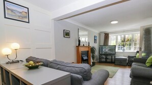 A modern living room with a grey sectional sofa, a small table with a bowl of fruit, a flat-screen TV, and a fireplace. - The Old Mill (Grange-over-Sands)