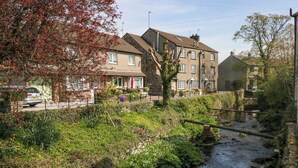A residential area with a narrow stream, houses with stone facades, and a parked car. - The Old Mill (Grange-over-Sands)