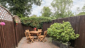 A patio with a wooden table and chairs, surrounded by a brick floor and a wooden fence. - Sunnyside Cottage (Filey)