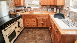 A kitchen with wooden cabinets, a stove, a microwave, a toaster, and a sink. - Sunnyside Cottage (Filey)