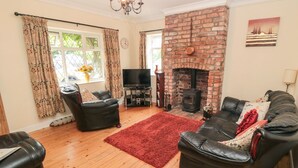 A living room with a brick fireplace, leather sofas, a red rug, and a television. - Sunnyside Cottage (Filey)
