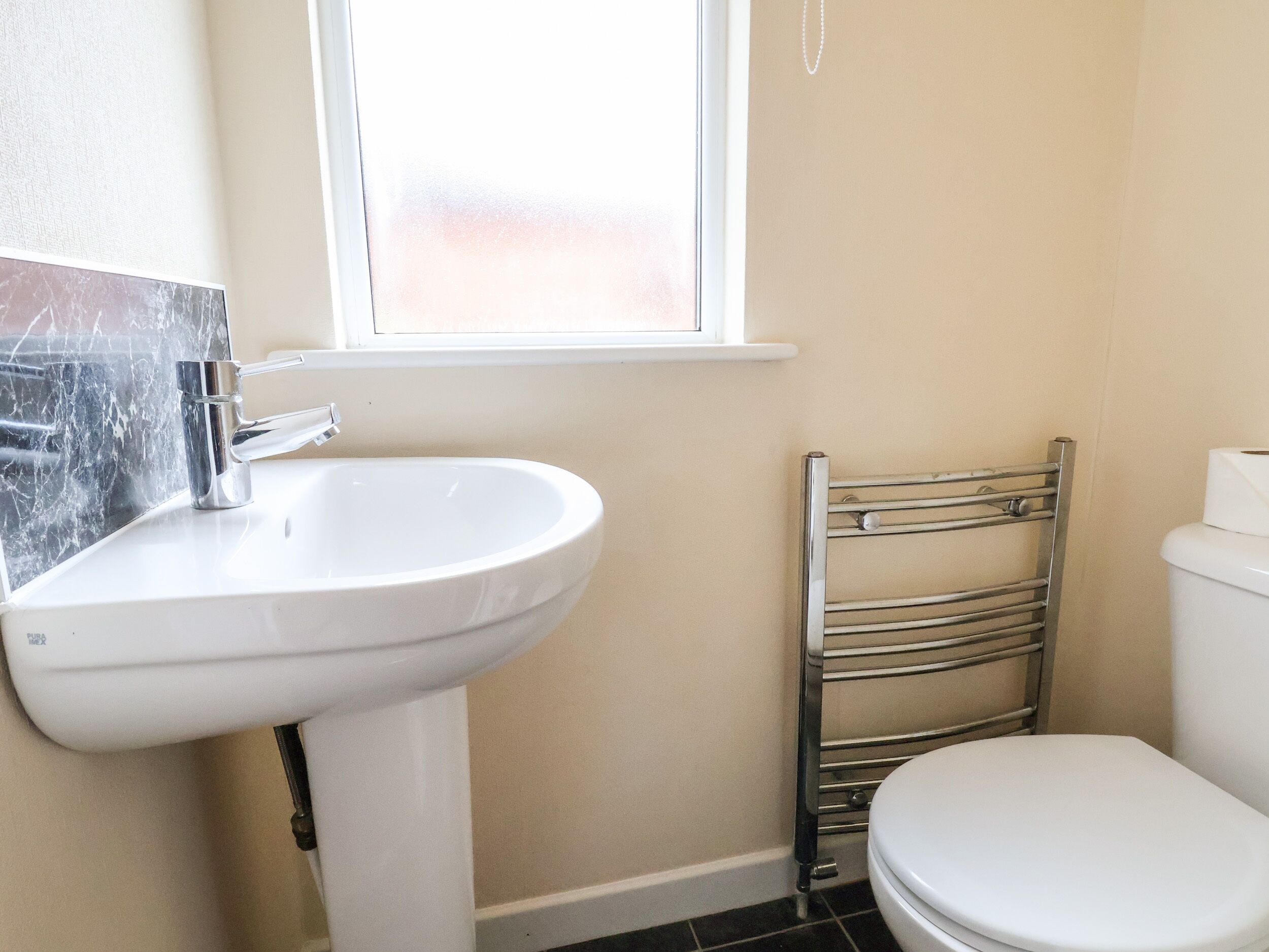 A bathroom with a white sink, a toilet, and a window above the sink.