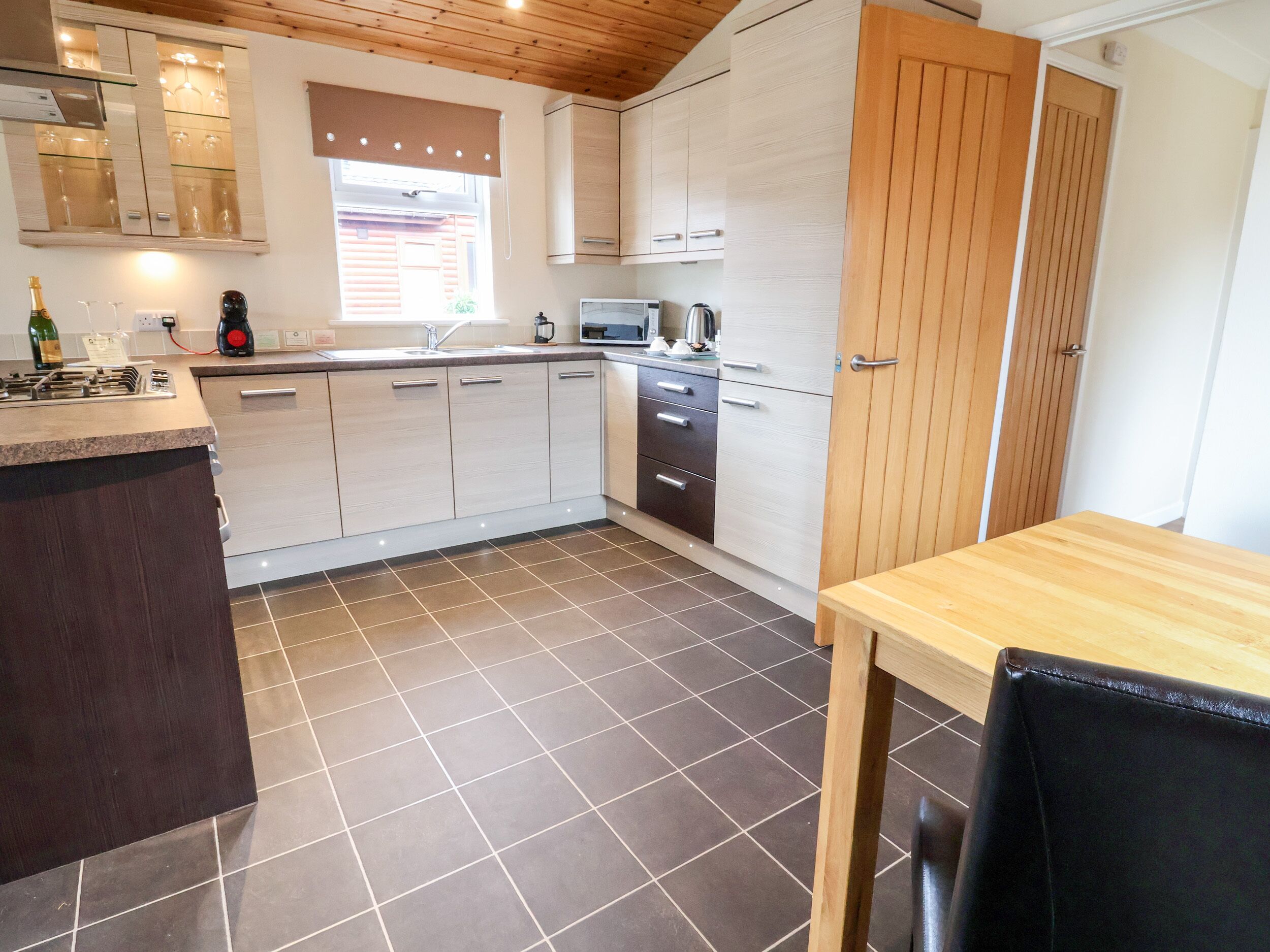 Una cocina moderna con una isla central, piso de baldosas oscuras y muebles de madera.