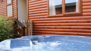 Un jacuzzi frente a una cabaña de madera con una escalera de madera y un ventanal pequeño.