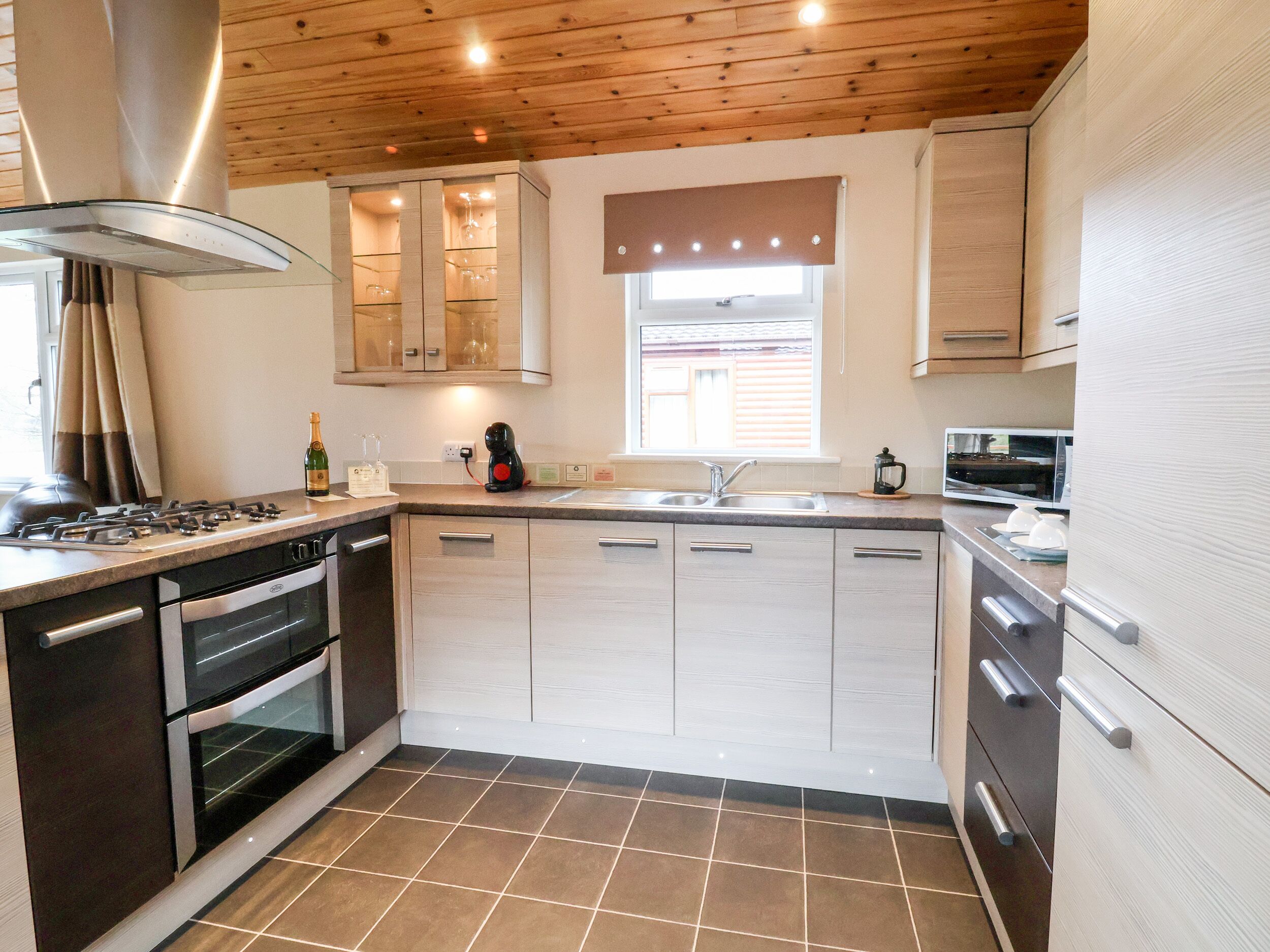 A modern kitchen with a gas stove, oven, and microwave. There is a window with blinds and a sink with a faucet.