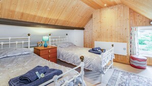 A cozy attic bedroom with two beds, wooden ceiling, and a window with curtains. - Duck Cottage (Bridlington)