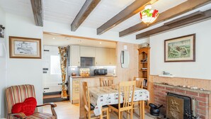 A cozy living room with a fireplace, a dining table with chairs, a striped armchair, and a kitchen in the background. - Duck Cottage (Bridlington)