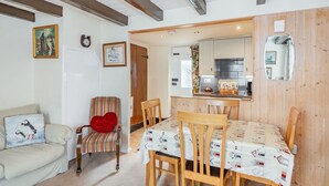 A cozy living room with a sofa, a striped chair, and a dining table set with a patterned tablecloth. - Duck Cottage (Bridlington)