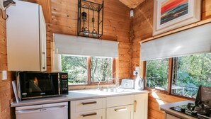 A compact kitchen with wooden walls, a microwave, a toaster, and a sink. - The Log Cabin (Oban)