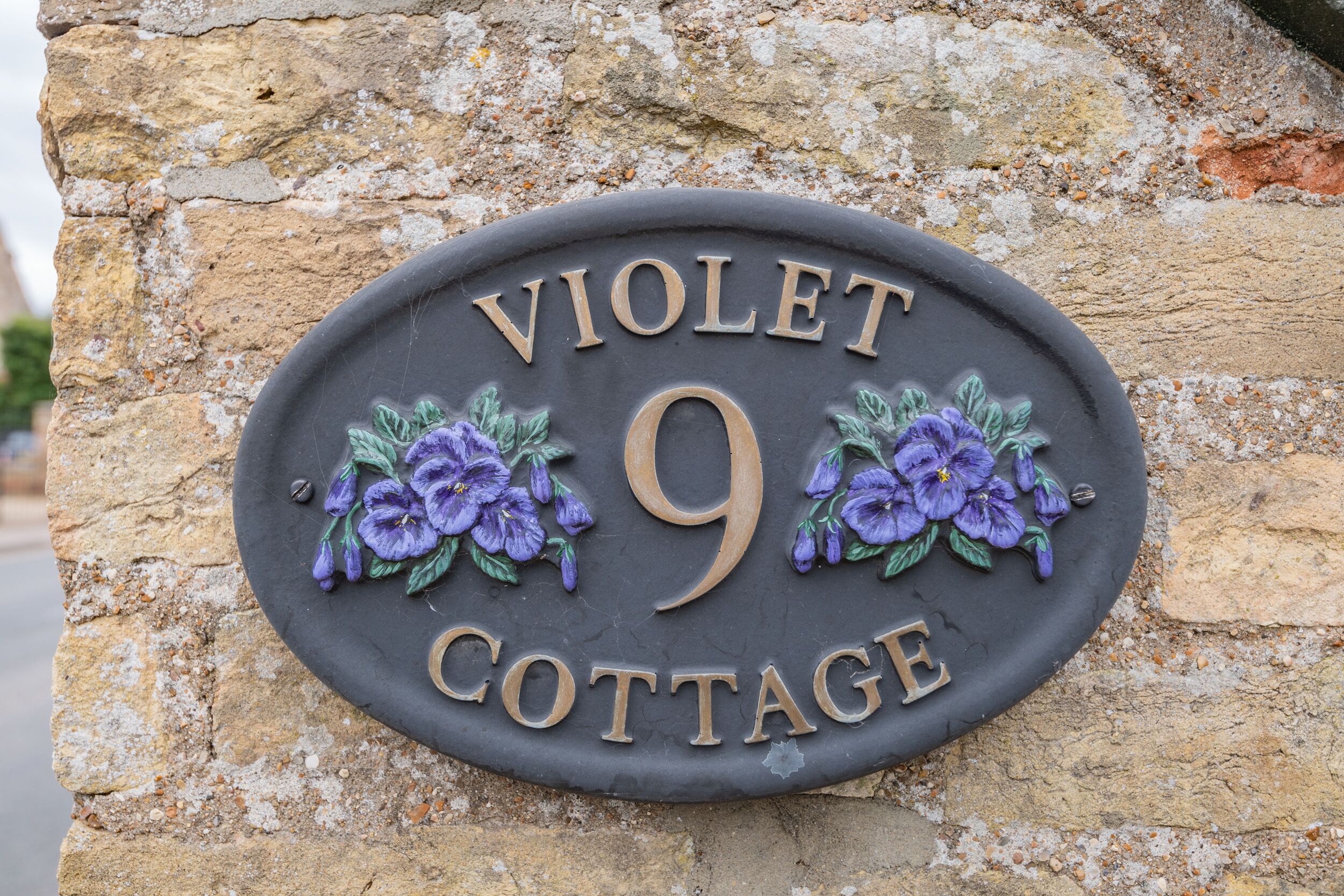 Letrero de Violet Cottage, con un fondo de pared de piedra y adornos florales.