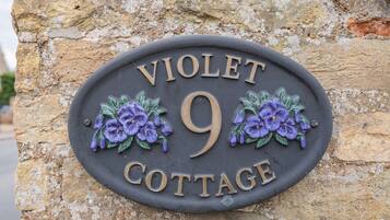 Letrero de Violet Cottage, con un fondo de pared de piedra y adornos florales.