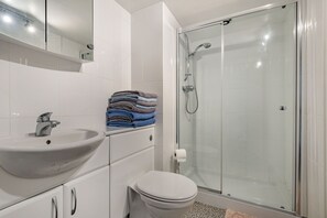 Een moderne badkamer met een douche in een glazen cabine, een wit wastafelmeubel en netjes opgevouwen handdoeken.