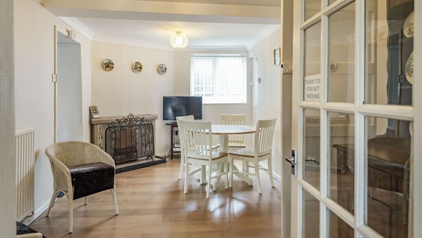 A dining area with a wooden table and white chairs, a fireplace, and a television. - Violet Cottage (Thetford)
