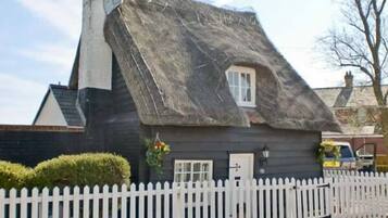 A traditional thatched-roof house with a white picket fence, a small window, and a door.