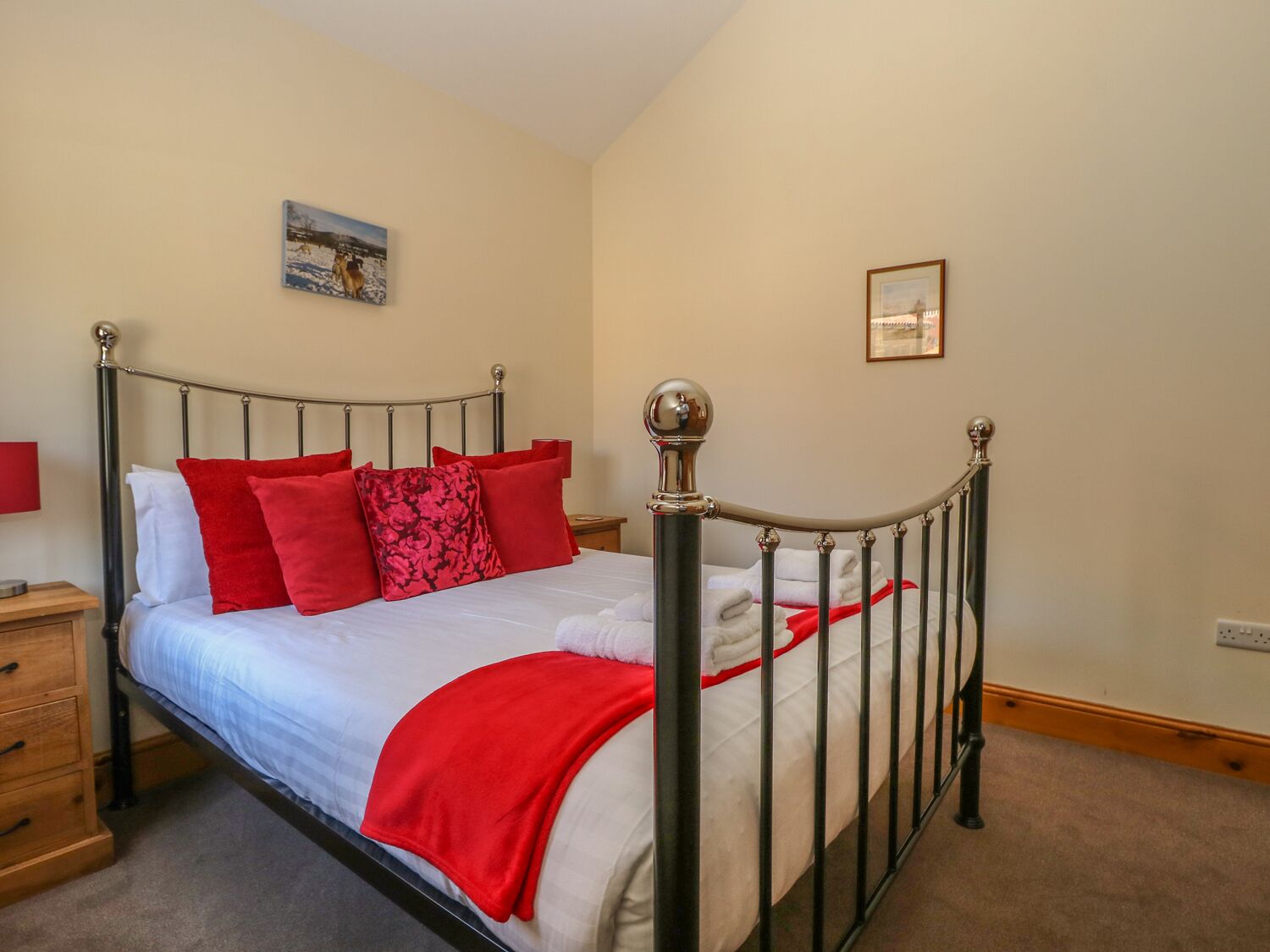 Ein ordentlich bezogenes Bett mit roter und weißer Bettwäsche, ein Nachttisch mit einer Lampe und ein Bild an der Wand.