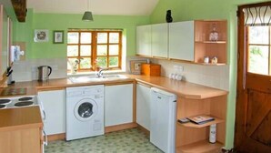 Une cuisine compacte équipée d’un lave-linge, d’un lave-vaisselle et d’un évier. Une fenêtre laisse entrer la lumière naturelle et une porte donne accès à l’extérieur.