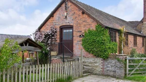 Une maison de campagne traditionnelle en pierre, avec une cheminée en briques, une porte en bois et une allée gravillonnée.