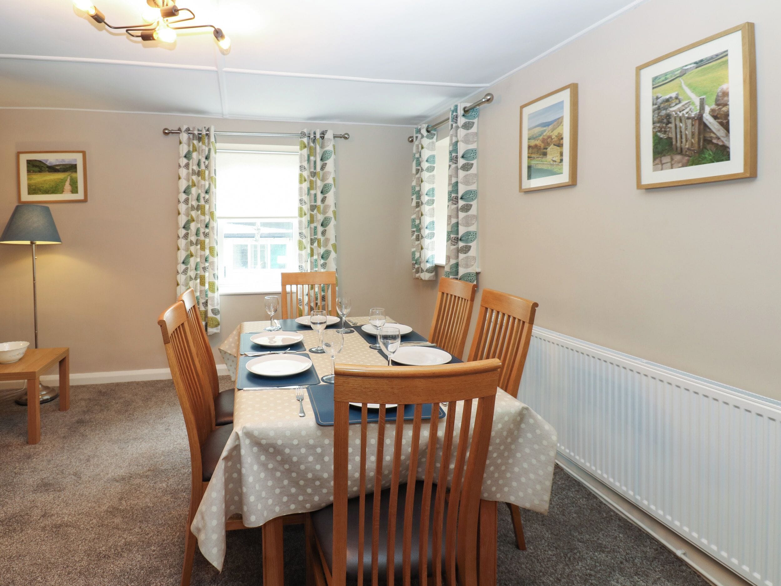 Une salle à manger avec une table mise pour quatre personnes, des chaises en bois, une lampe et deux tableaux encadrés accrochés au mur.
