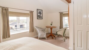 A bedroom with a large bed, two chairs, a small table, and a door.