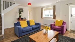 A living room with a blue sofa, a purple armchair, a wooden coffee table, and a red pendant light.