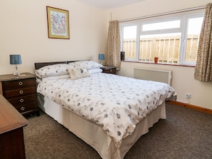 A bedroom with a bed, a nightstand, a lamp, a dresser, a radiator, and a window with curtains.