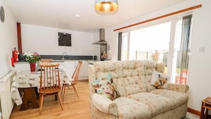 Una sala de estar con un sofá floral, una mesa de comedor de madera, sillas y una cocina al fondo.
