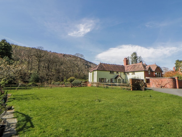 A house with a fenced yard, a pathway, and a hill in the background.
