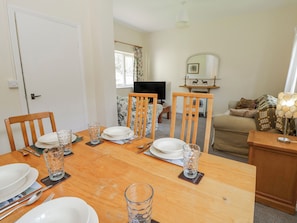 A dining area with a wooden table set for four, chairs, and a television in the background.
