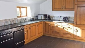 A kitchen with wooden cabinets, a stove, and a microwave. - The Stables (Hope Valley)