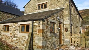 A stone building with a pitched roof, a small porch, and a wooden gate. - The Stables (Hope Valley)