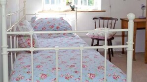 Un dormitori amb un llit individual, roba de llit floral, una cadira de fusta, un escriptori i una finestra amb vista a vegetació.