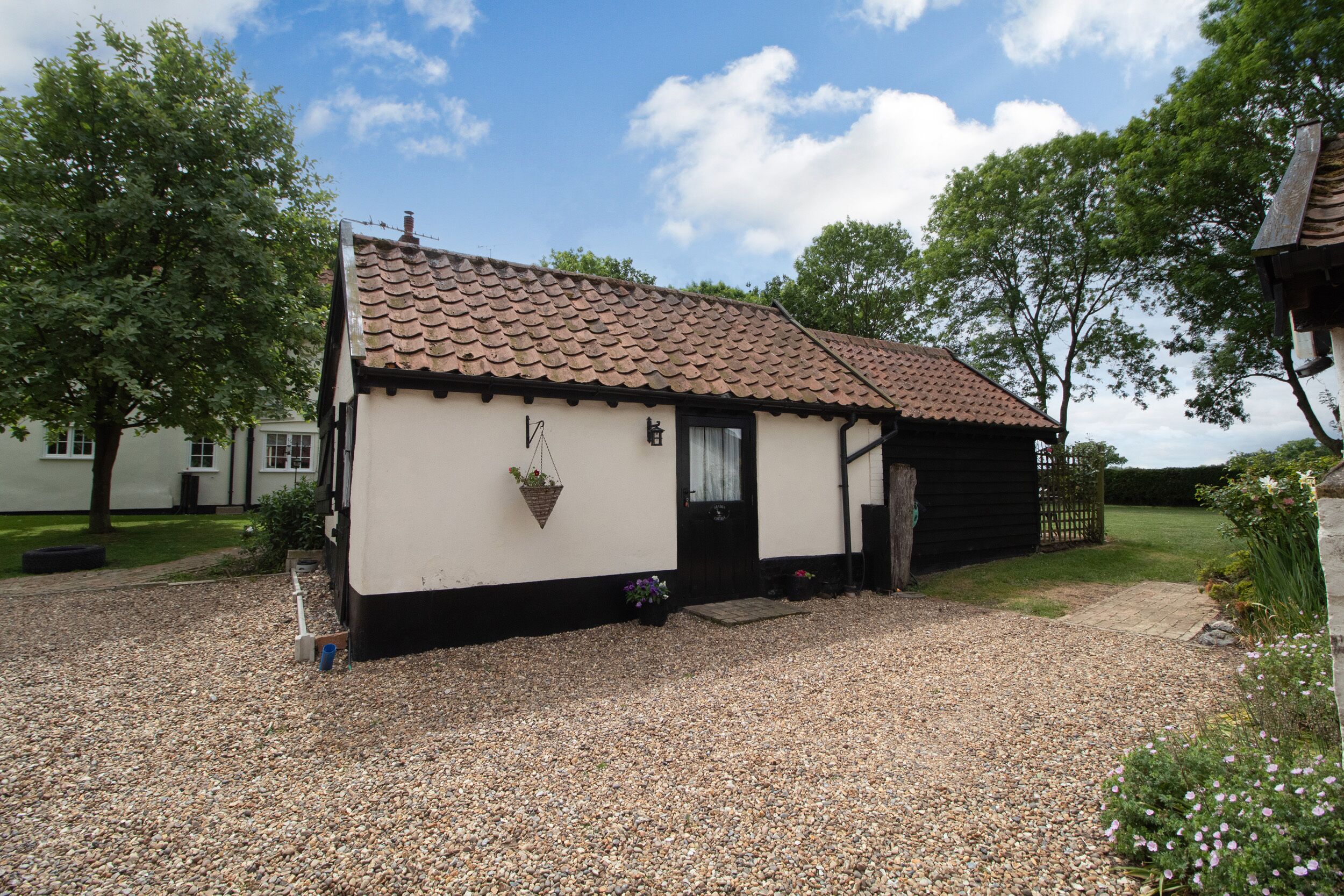 A small, single-story building with a tiled roof, a black door, and a gravel driveway.