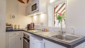 A kitchen with white cabinets, a microwave, a sink, and a window with a vase of flowers.