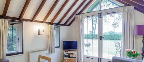 A room with a TV, a table, a sofa, and a window with curtains.